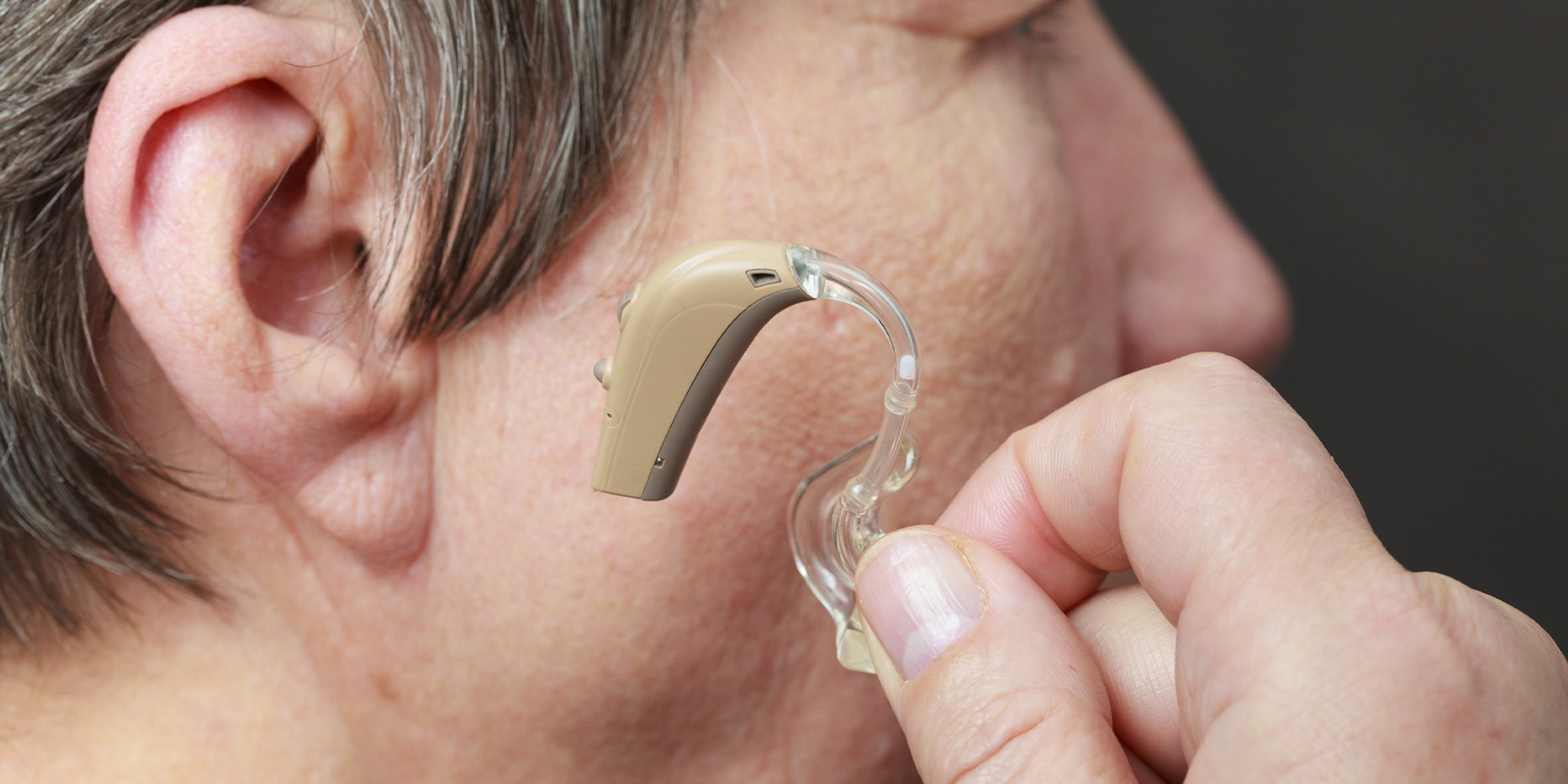 woman holding hearing aid up next to ear