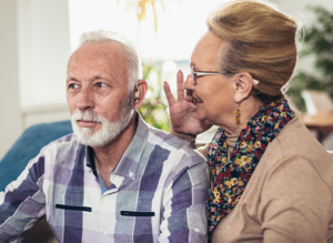 elderly woman yelling into elderly husbands ear